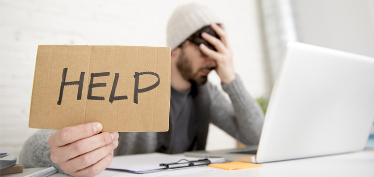 Junger verzweifelter Mann mit „Help“-Schild vor einem Laptop.