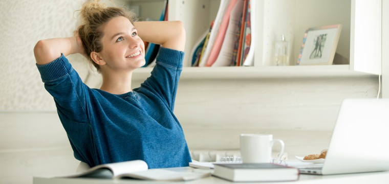 Fernstudium-Kosten – eine Frau sitzt lächelnd am Schreibtisch.
