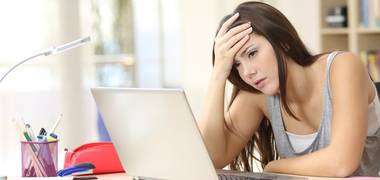 Junge Frau sitzt frustriert am Schreibtisch vor Laptop